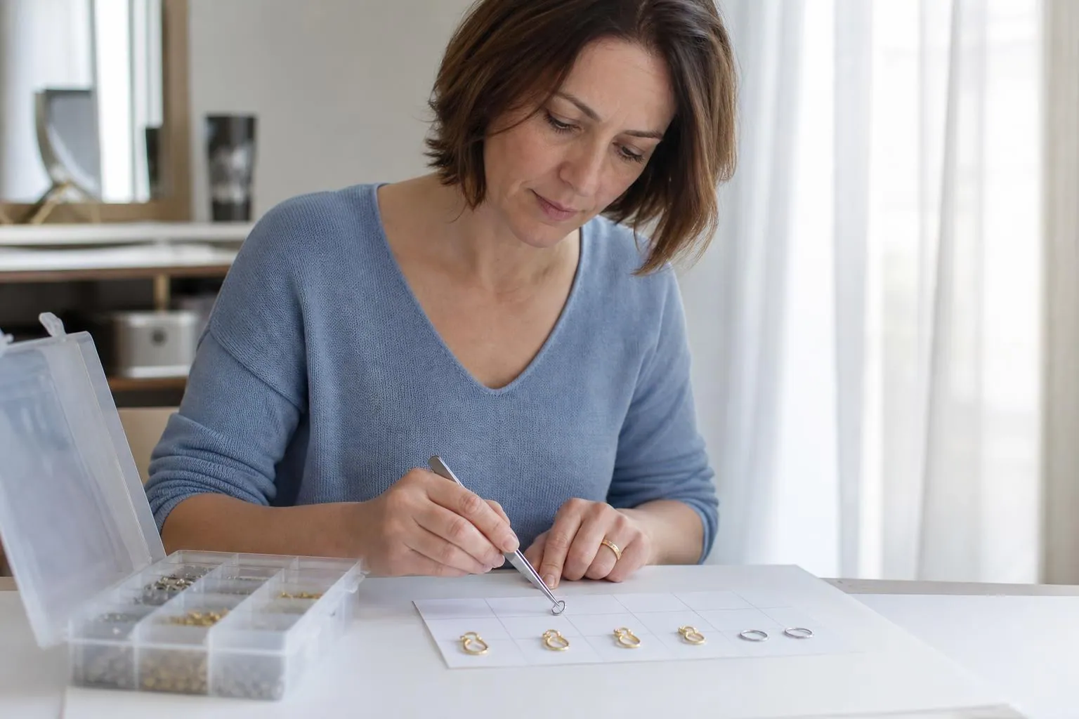 Créatrice de bijoux fantaisie comparant des crochets d’oreille en acier et des fermoirs en laiton sur une feuille de classement blanche