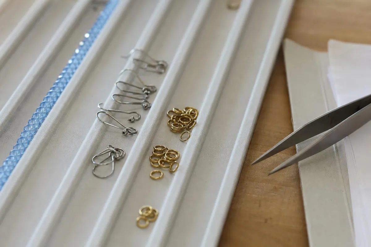 Gros plan d’une planche à perles rainurée avec crochets d’oreille en acier, perles de verre et pochette de documents fournisseur agrafés